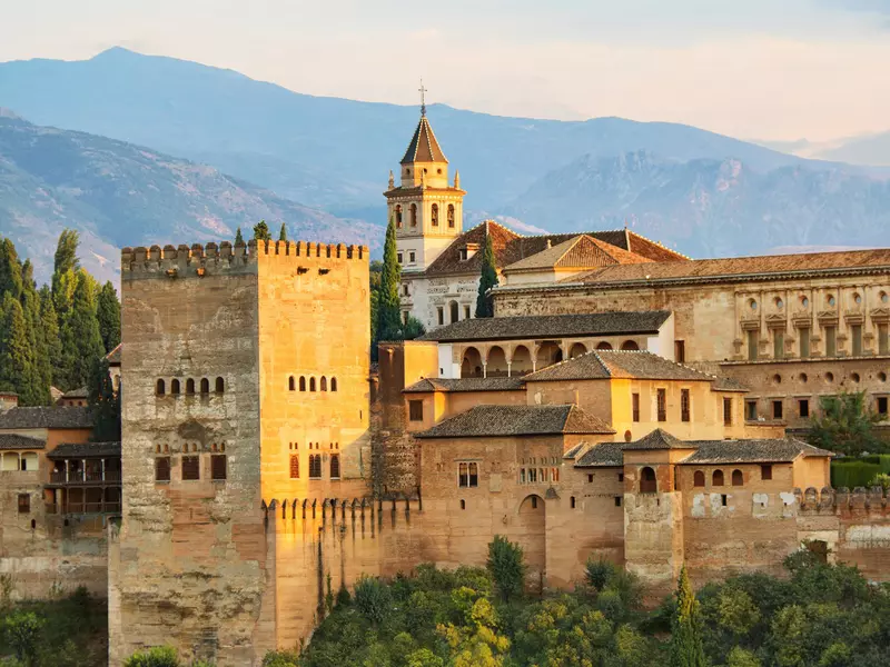 A Moorish castle sits on a lush hillside with mountains in the background. 