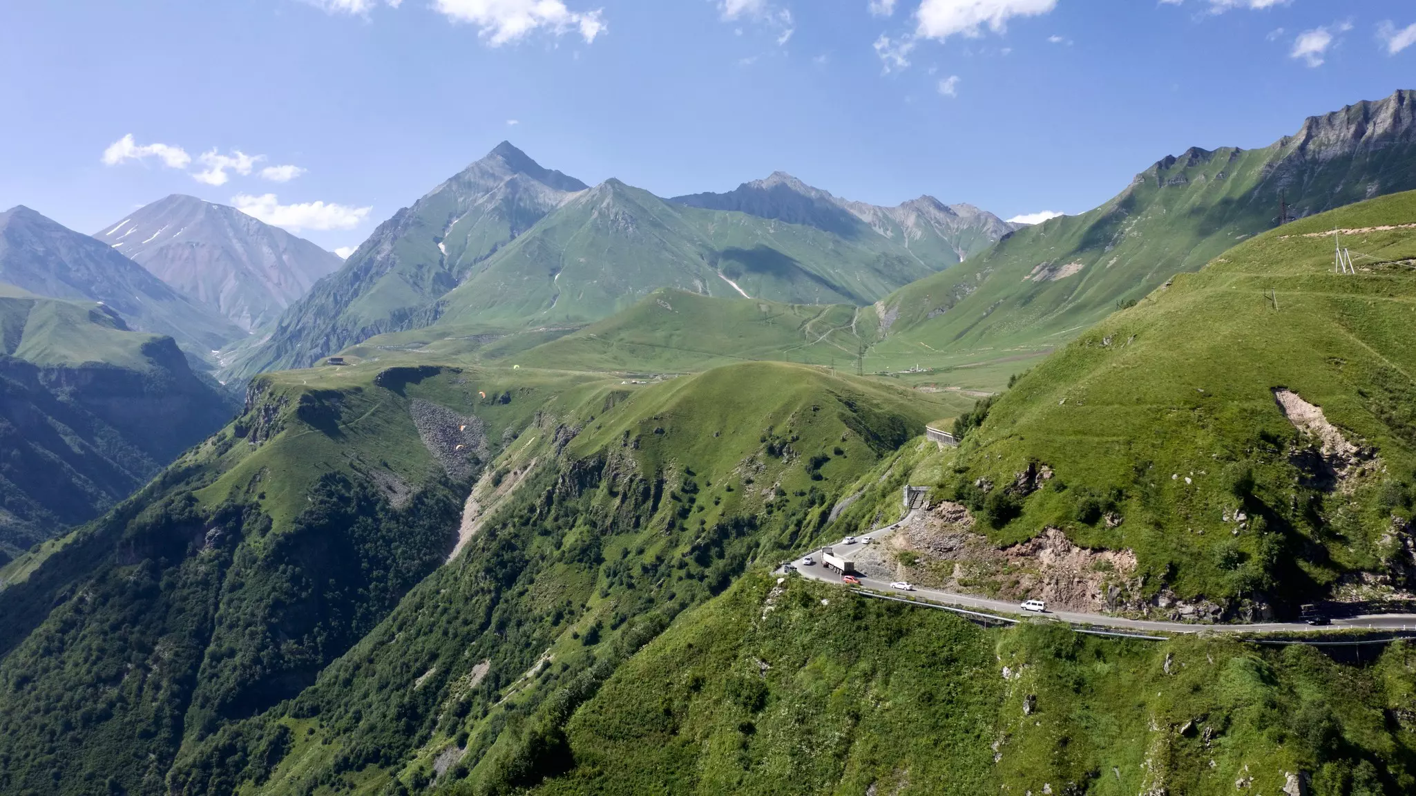 A ribbon of road skirts the slopes of steep mountains covered in greenery.