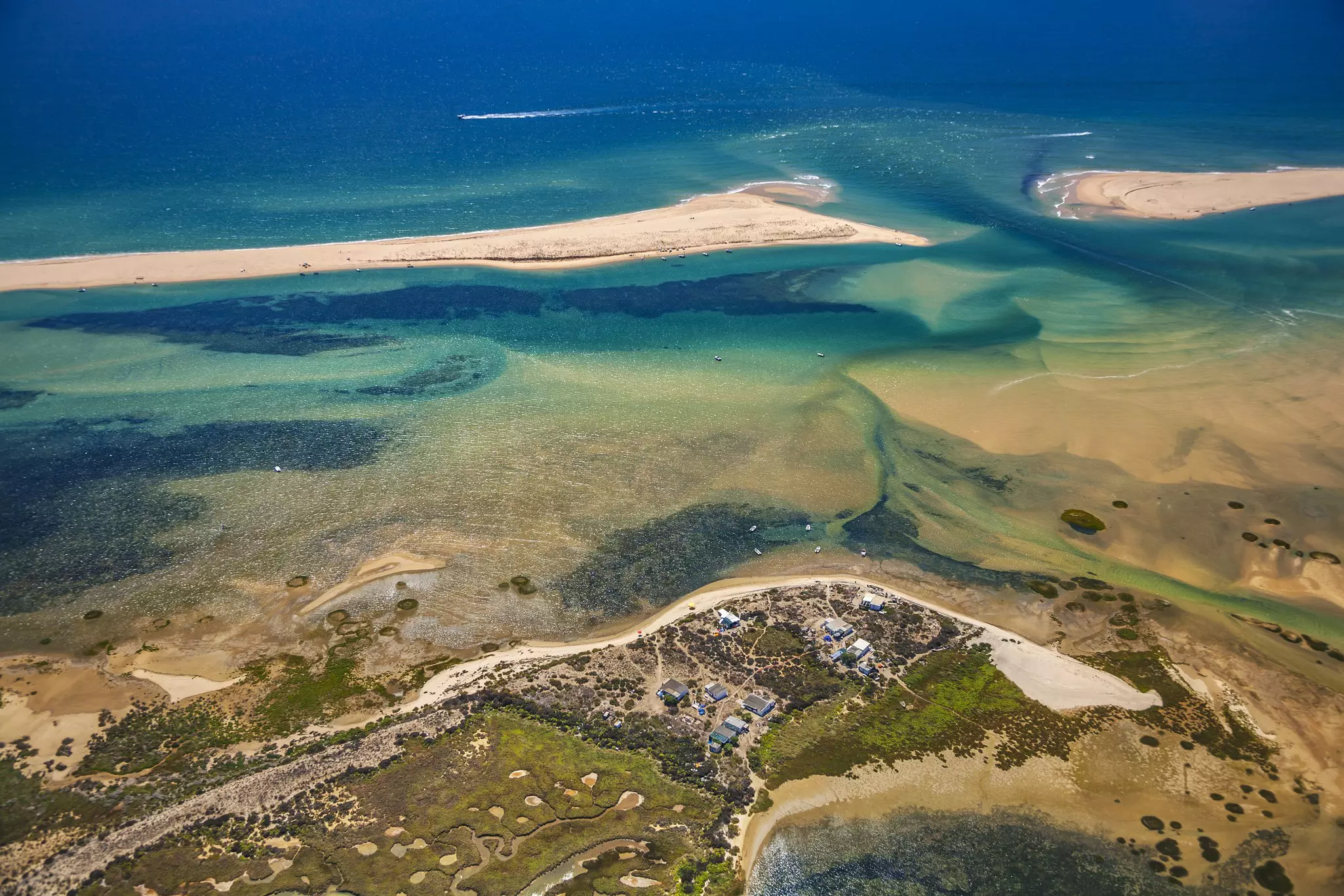 An aerial view of the ocean with a grassy spit in the foreground and a sandy spit further out in the water.