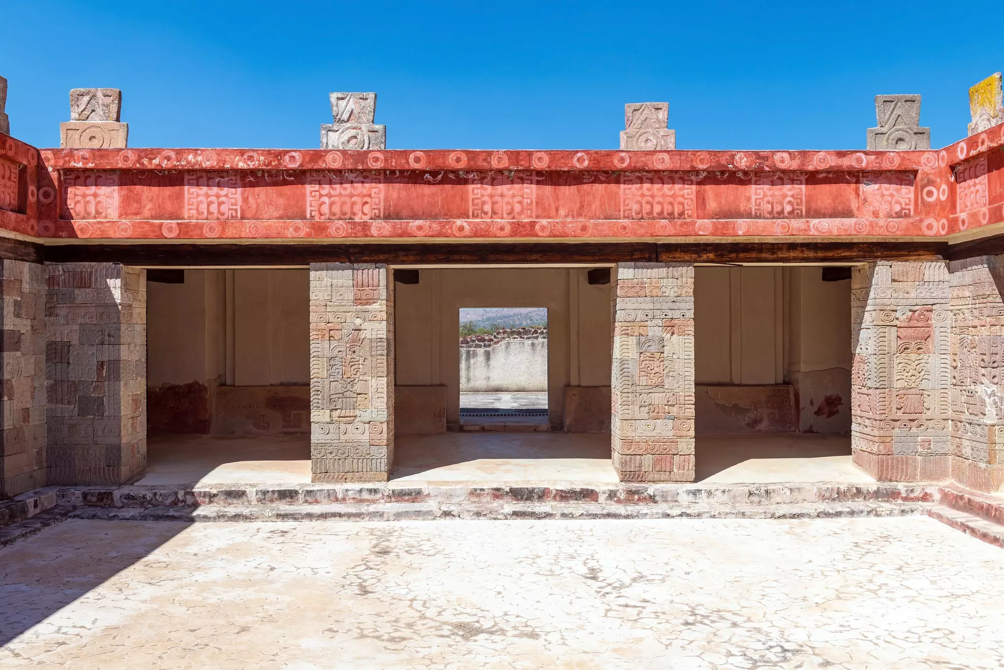 View of an inner courtyard of a temple with red fresco and carvings on the stone columns on a sunny day.