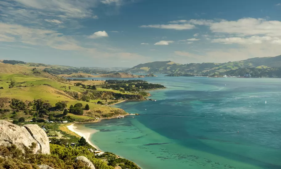 Otago Harbour near Dunedin from a rocky hilltop, a sandy cove and green farmland curving along turquoise water