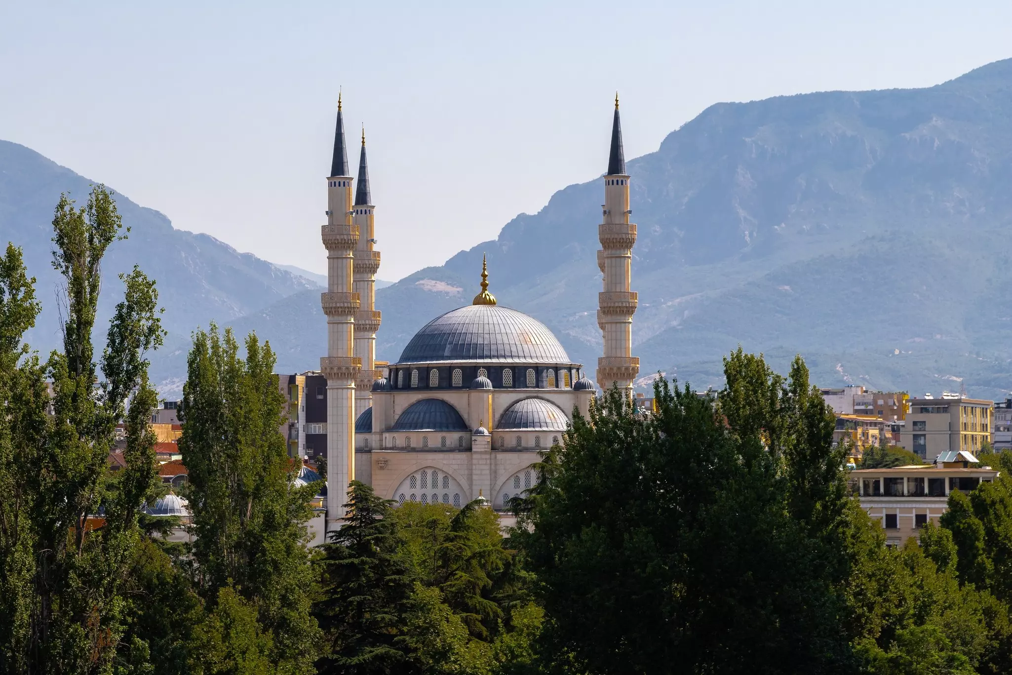 The dome and minarets of a mosque are pictured amon trees in an urban neighborhood.