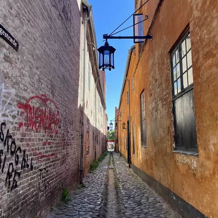 A shaded, narrow cobblestone lane between two buildings on a sunny day.