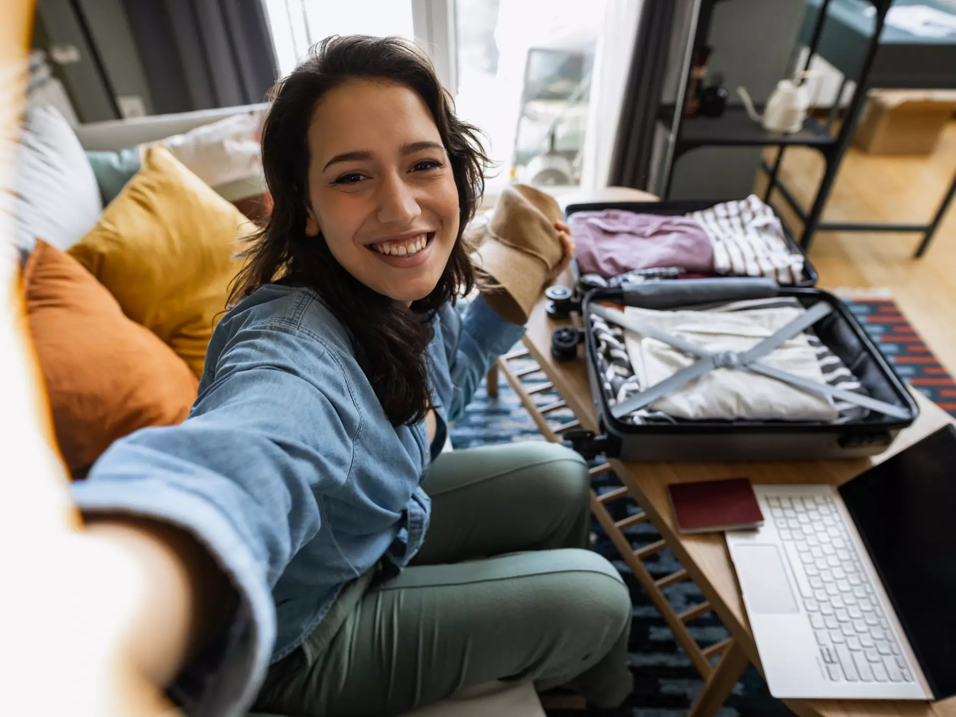 Young woman packing her suitcase and talking on a video call with her friends