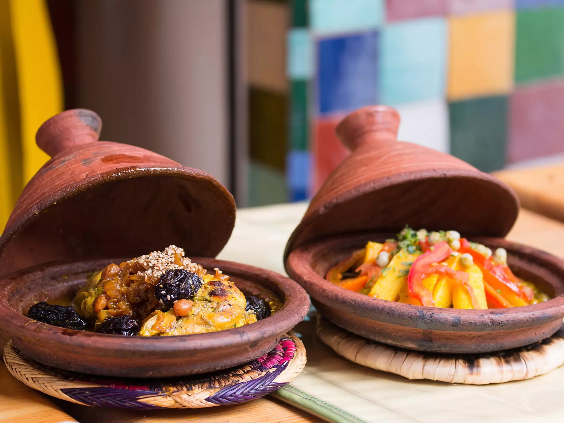 Two tajines next to each other on a table with vegetables and meat.