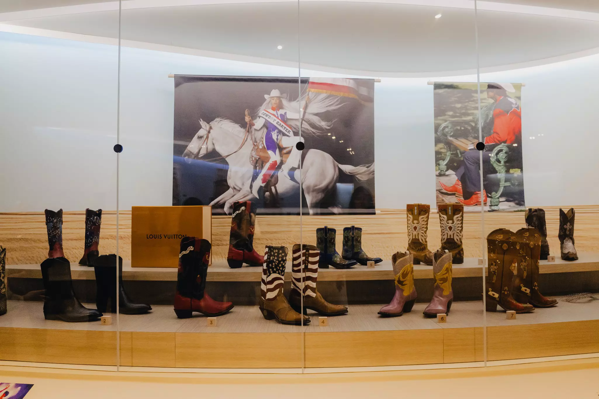 A glass museum case of cowboy boots on display.