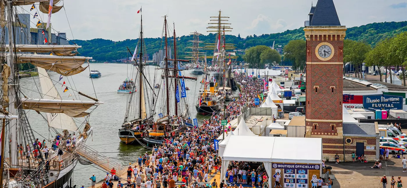Crowds gather on a busy quay to access historic sailing ships. 