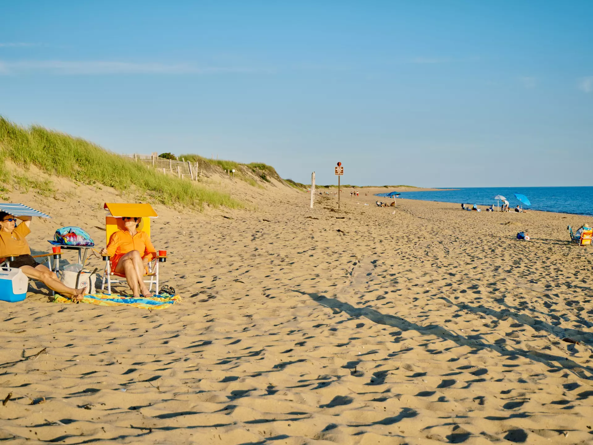 Two people sit in chairs on a sandy beach in late afternoon.