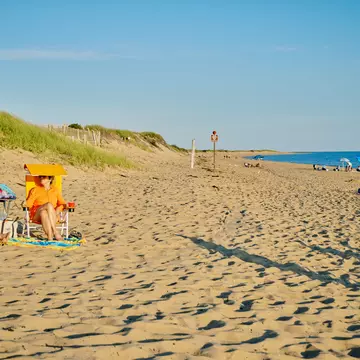 Two people sit in chairs on a sandy beach in late afternoon.