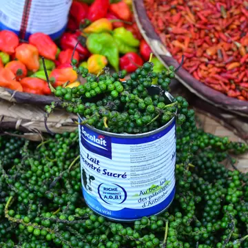 Bunches of fresh green peppercorns in a tin set in a woven basket beside baskets of red and orange chillies.