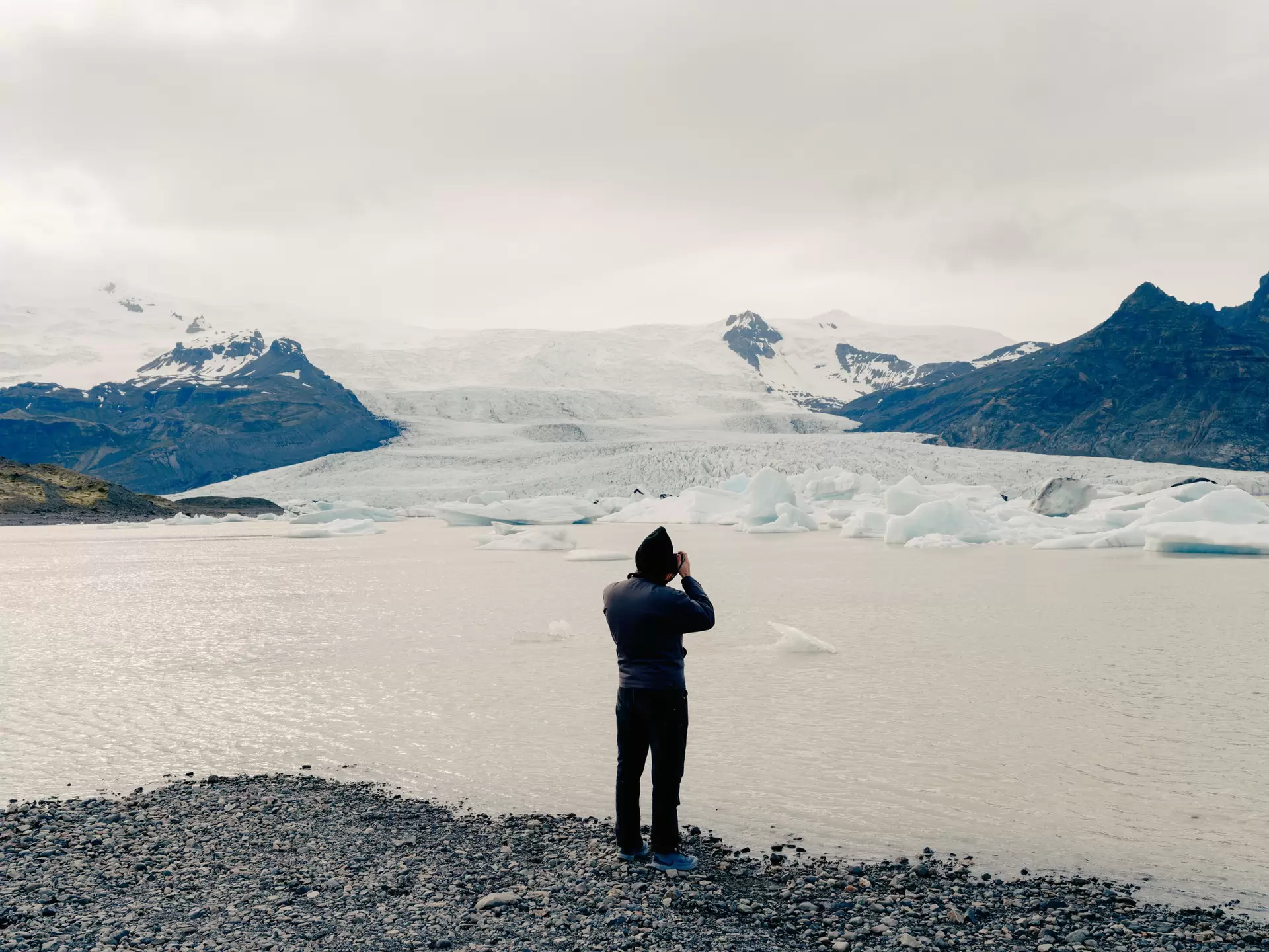 A man with back to camera is taking a photo of Fjallsárlón Lake and Lagoon in Iceland