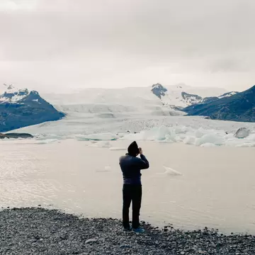 A man with back to camera is taking a photo of Fjallsárlón Lake and Lagoon in Iceland