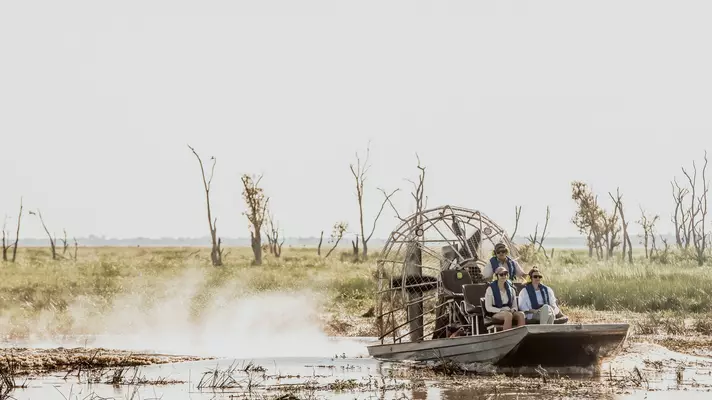 People on an airboat through a marshy area.