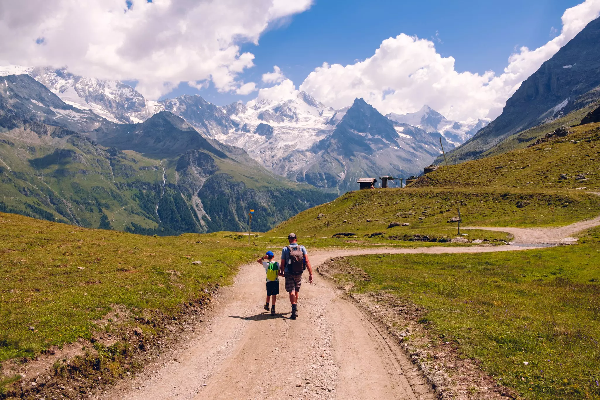 Grandfather and grandson enjoy a great view while hiking a mountain trail high in the Pennine Alps in summer, rear view. Valais, Switzerland. 