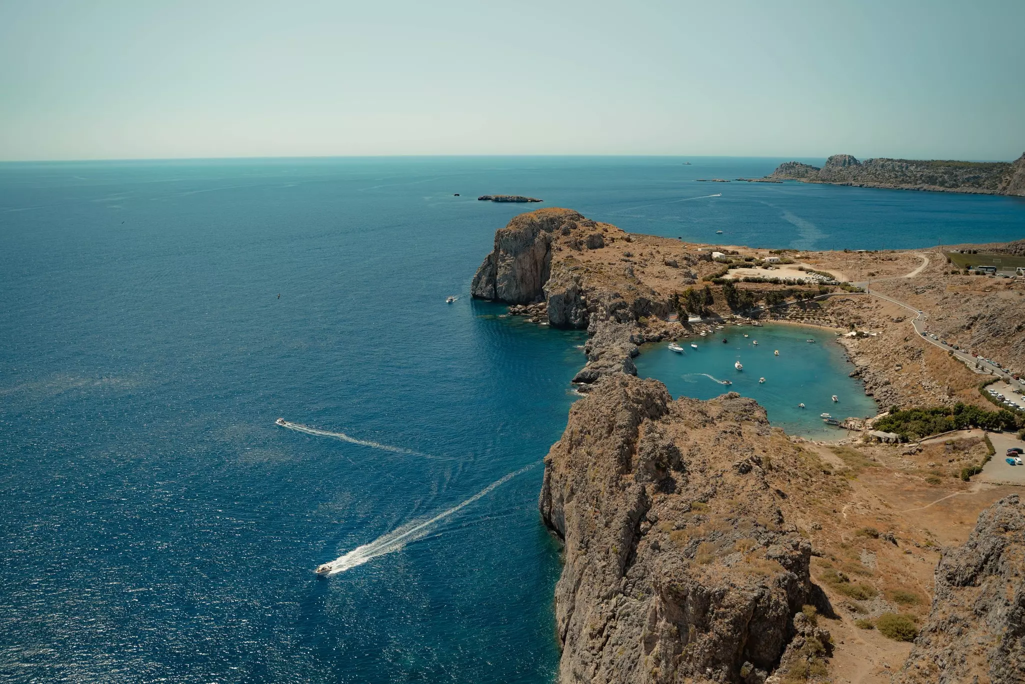 A rocky coastline and bay filled with boats and lined with sunbeds