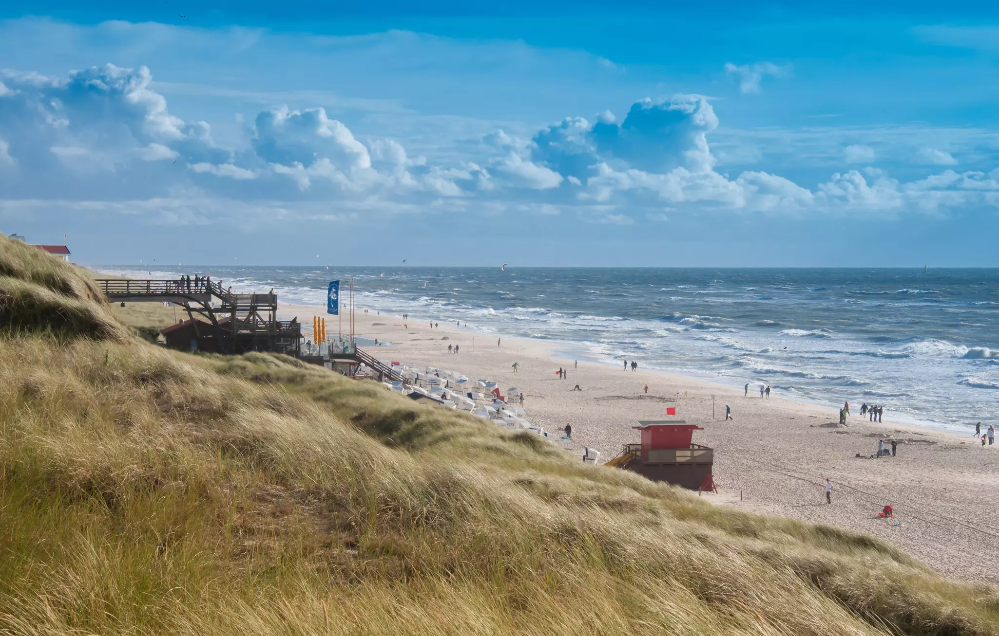 A busy beach lapped by large waves on a windy day.