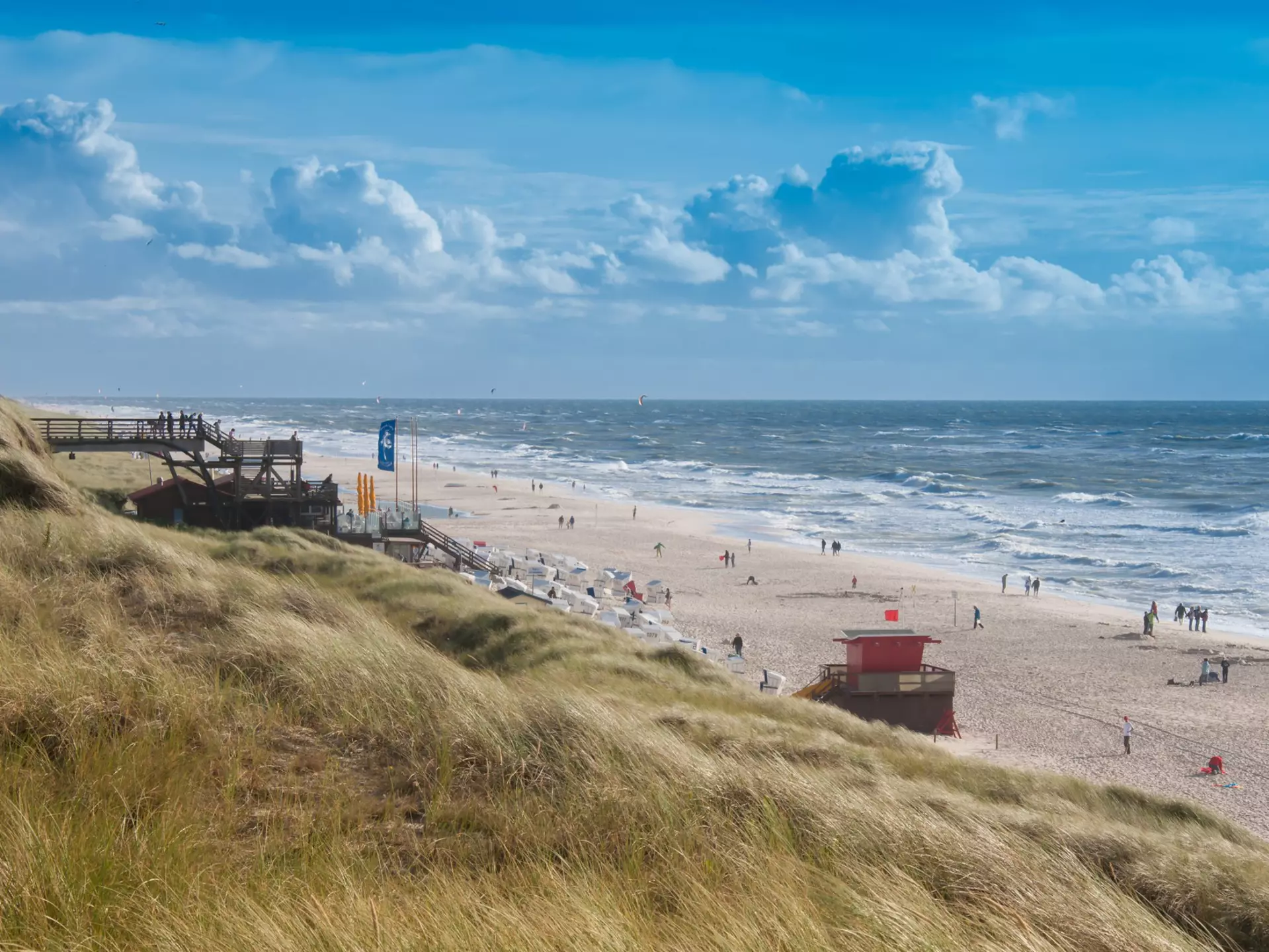 A busy beach lapped by large waves on a windy day.