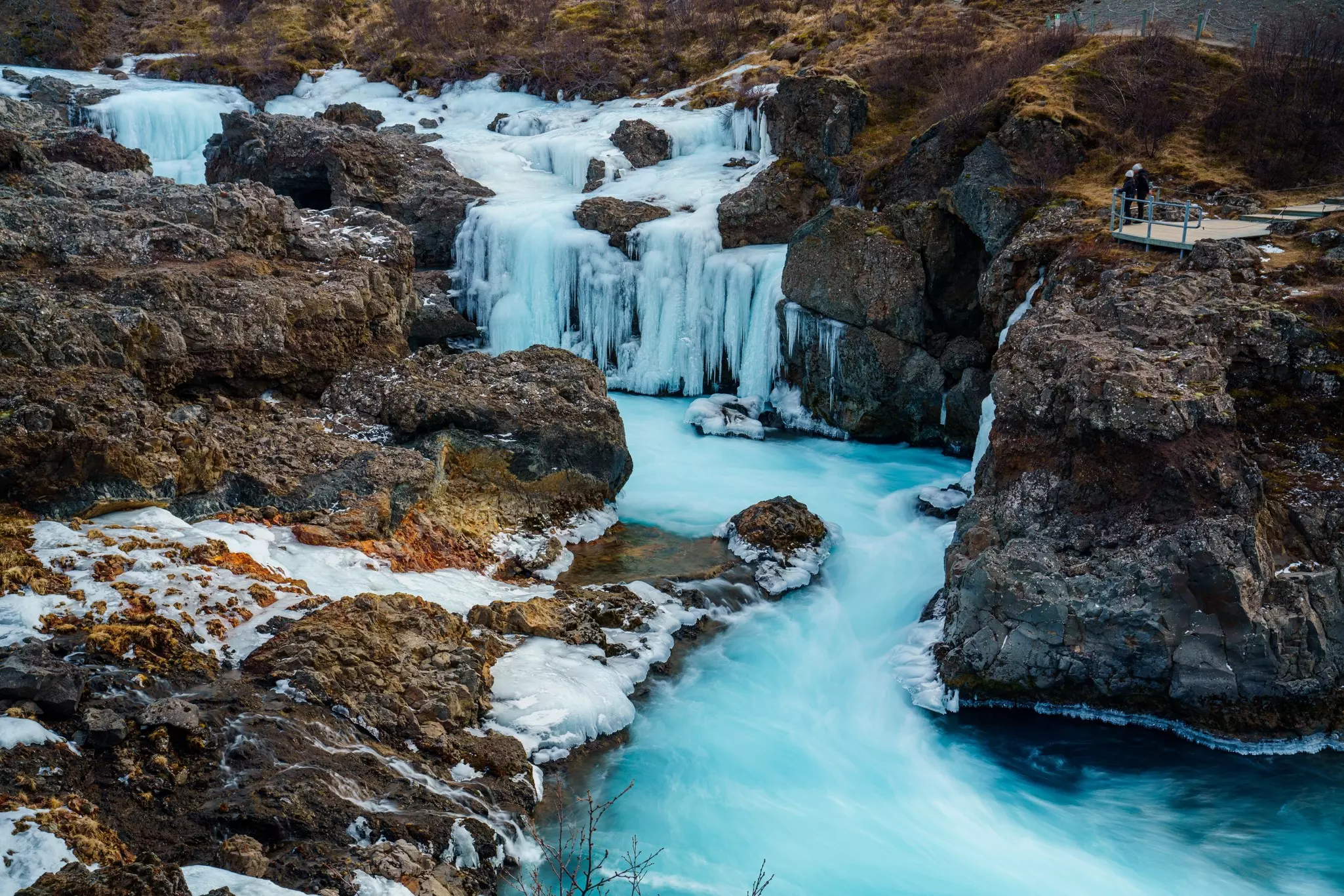 Two people stand on a platform looking towards a frozen waterfall