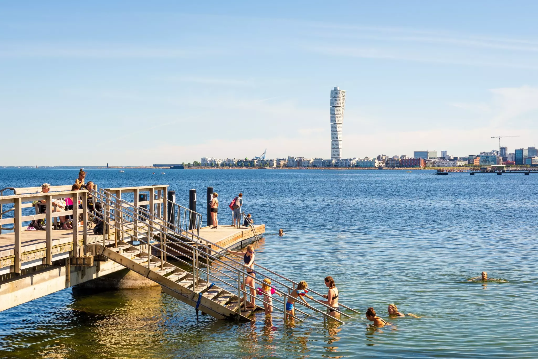 Malmö, Sweden - July 20, 2024: Adults, children and seniors enjoy sea bathing on a sunny summer day at the pier 6 of the Ribersborg beach, with a view over the Turning Torso tower., License Type: media, Download Time: 2025-02-13T14:49:27.000Z, User: Ppeterson948, Editorial: true, purchase_order: 56530 - Guidebooks, job: Global Publishing WIP, client: Global Publishing WIP, other: Pia Peterson Haggarty