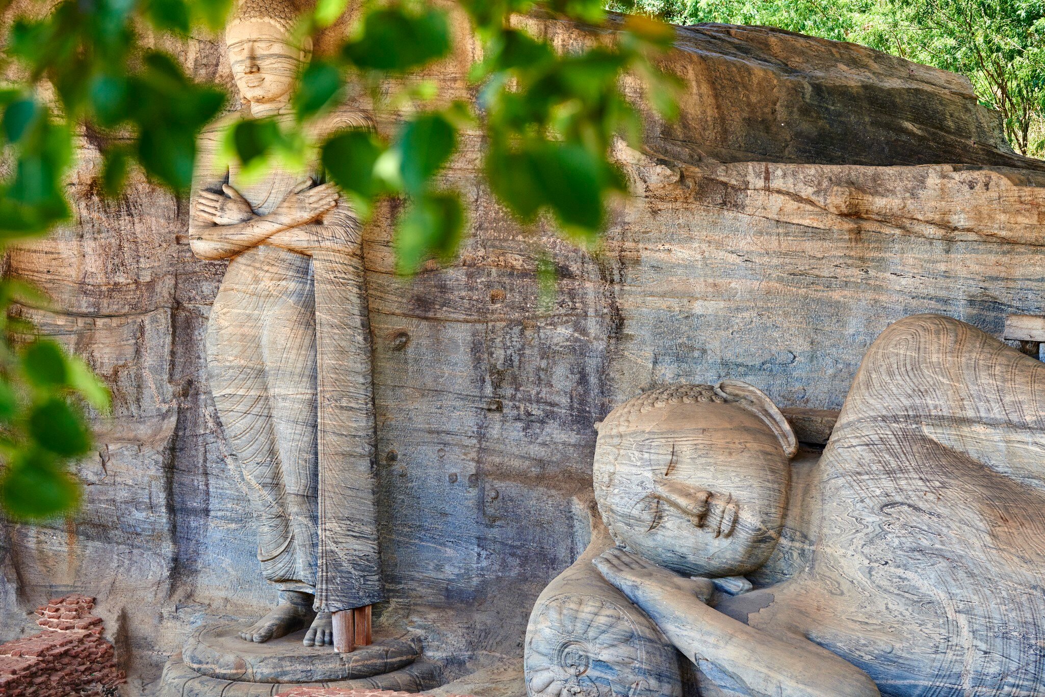 Monumental Buddha statues viewed through leaves.