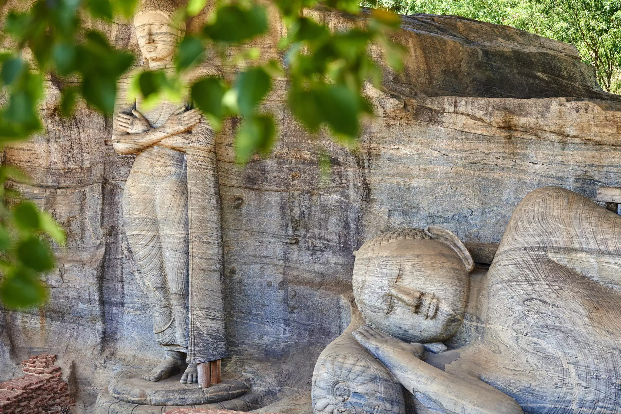 Monumental Buddha statues viewed through leaves.