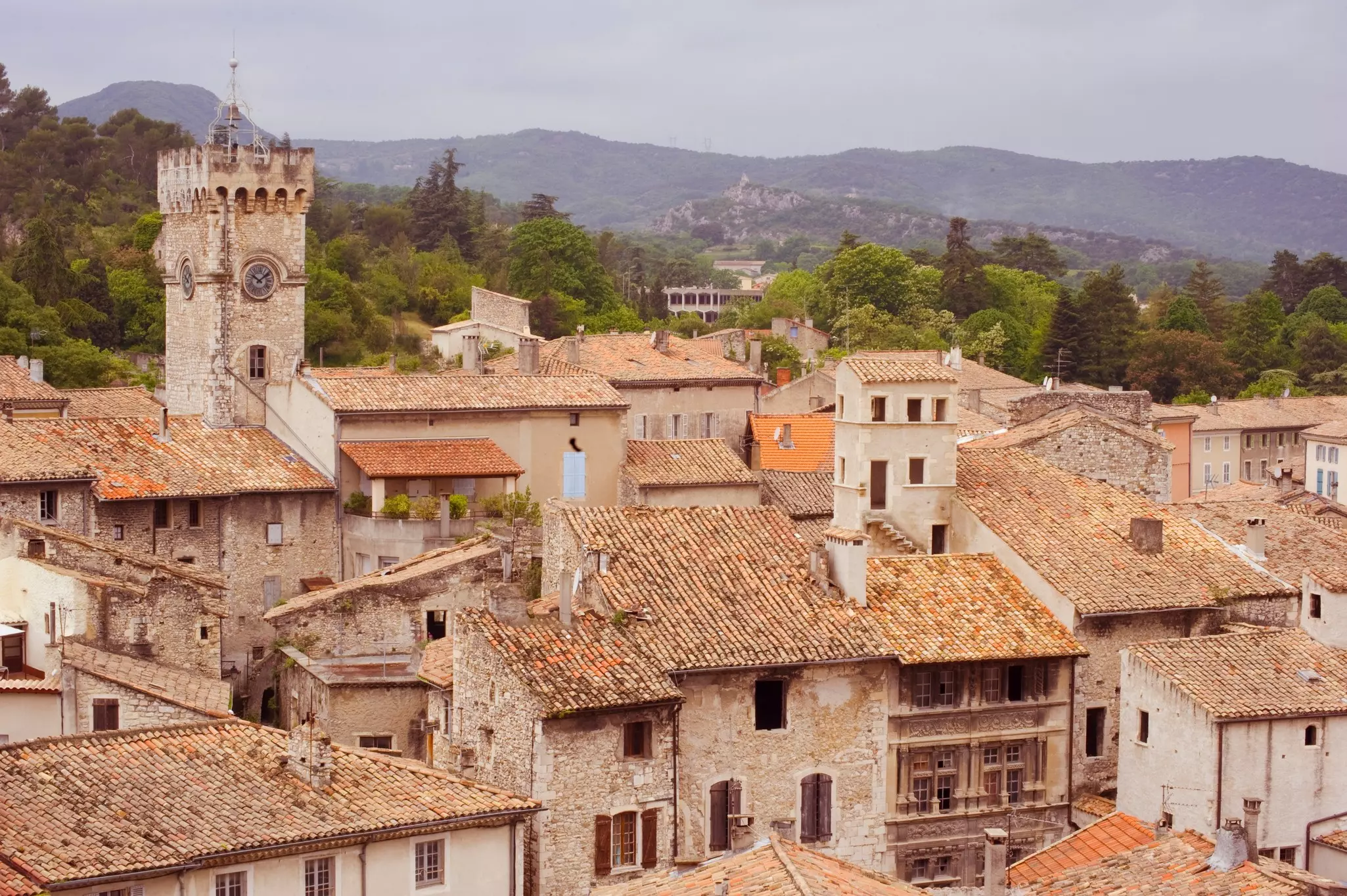 Tiled rooftops of old stone houses clustered close together in a village. A square church tower stands above them.
