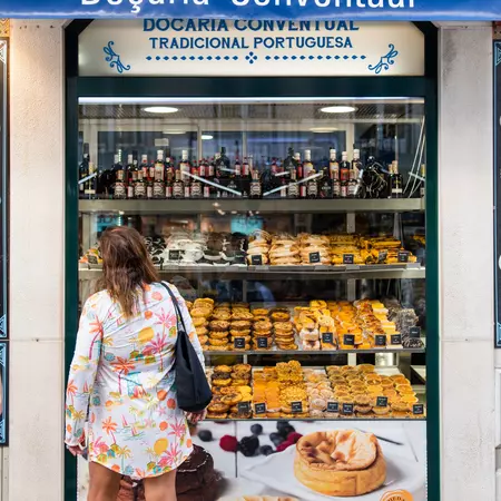 A woman stands in front of a window looking into a bakery window. 