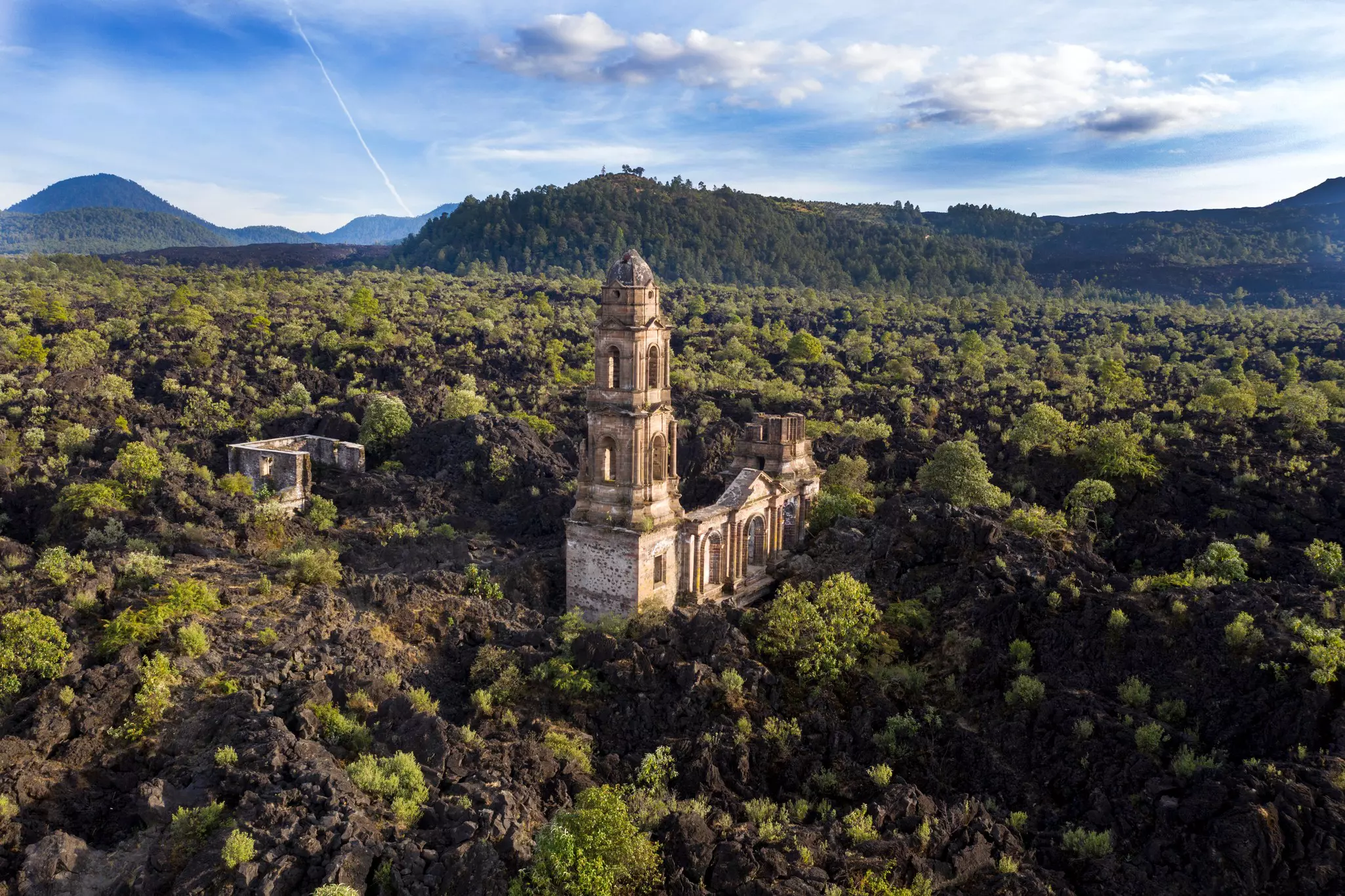 The ruins of a church belfry surrounded by woodland and a rocky volcanic landscape