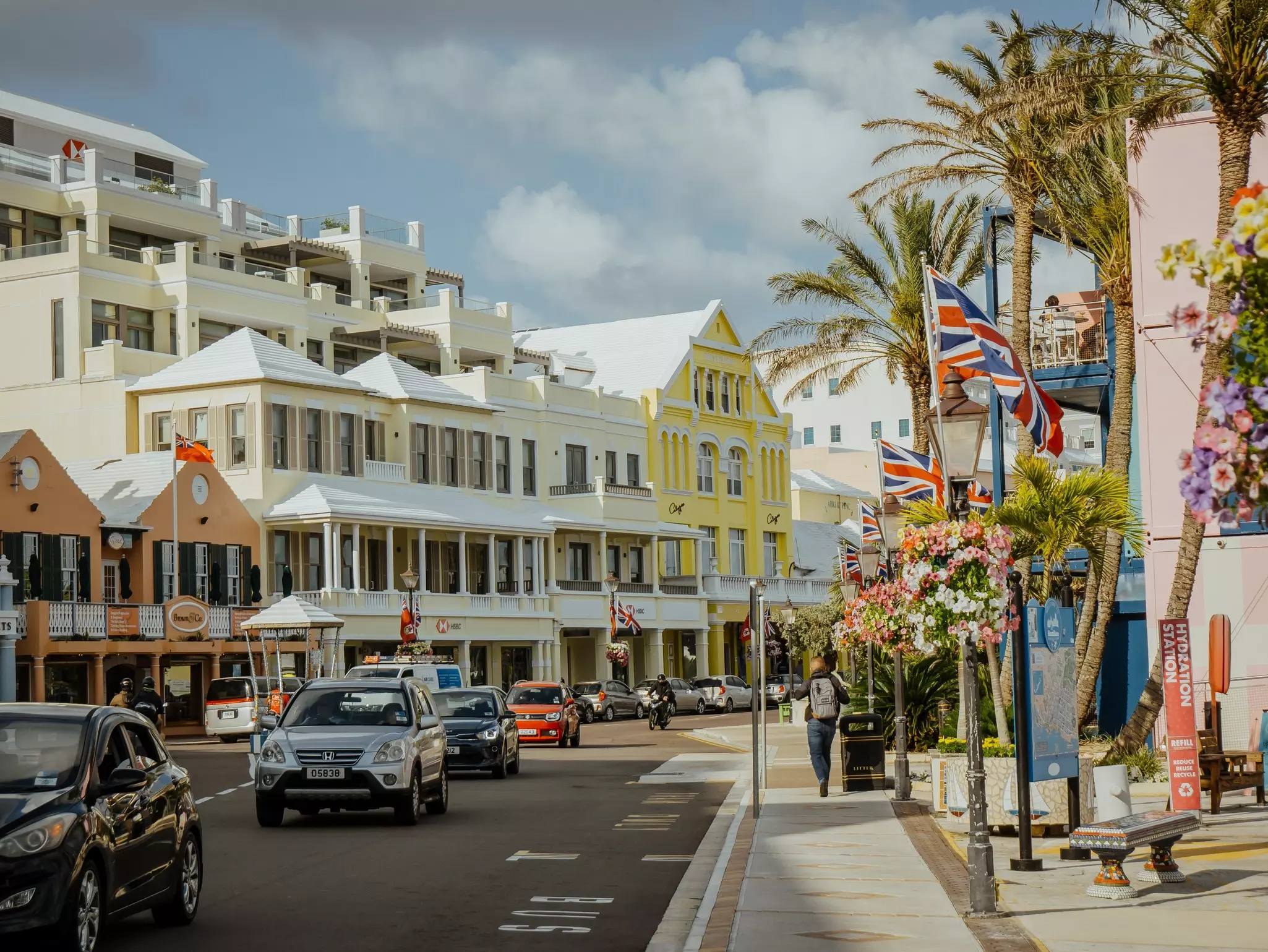 Cars drive on a city street past pastel-colored buildings decked in flags.