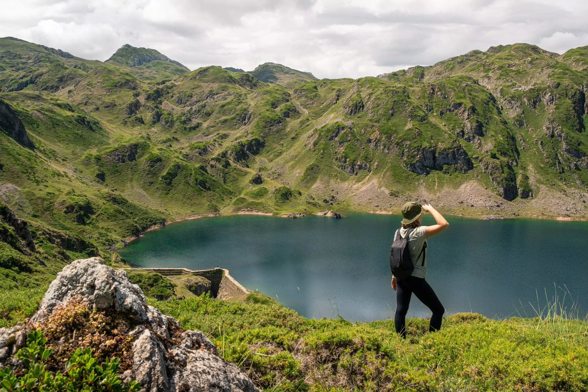 Young woman with a hat admiring the views of a mountain lake