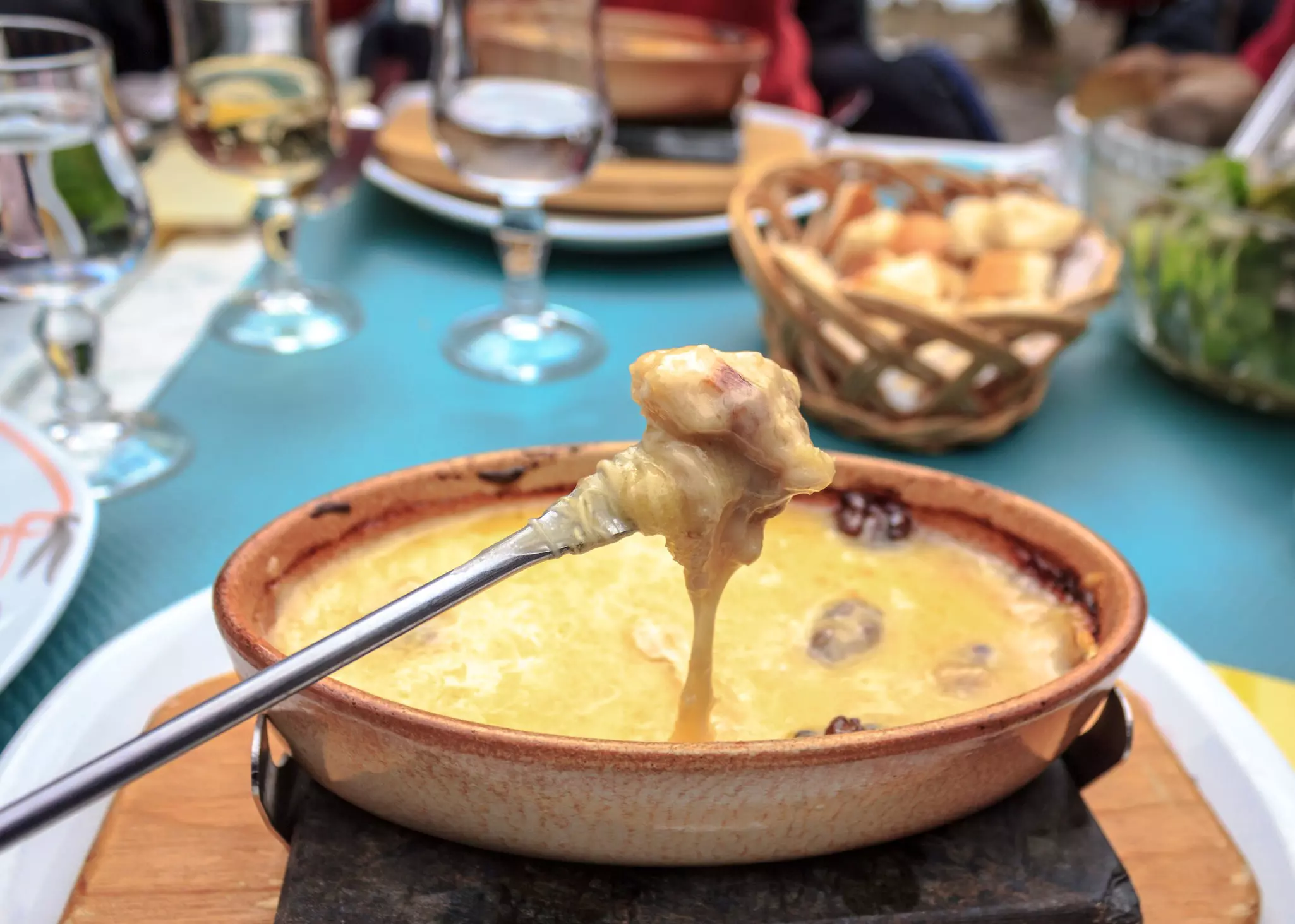 A long fork dips a hunk of bread into melted cheese in a clay pot