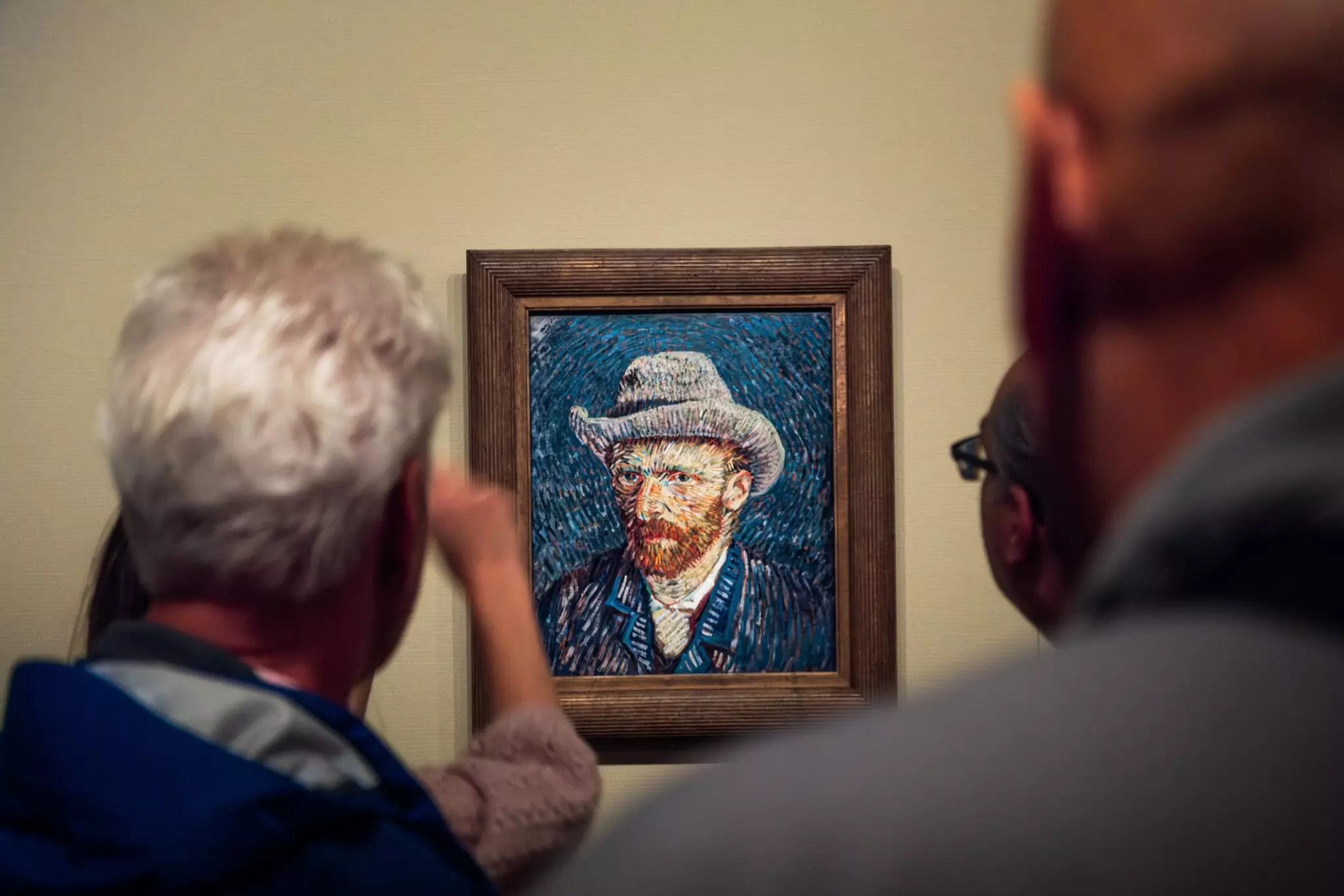 A tour guide speaks to visitors (seen from behind) on a small, brightly colored portrait hanging at a museum.