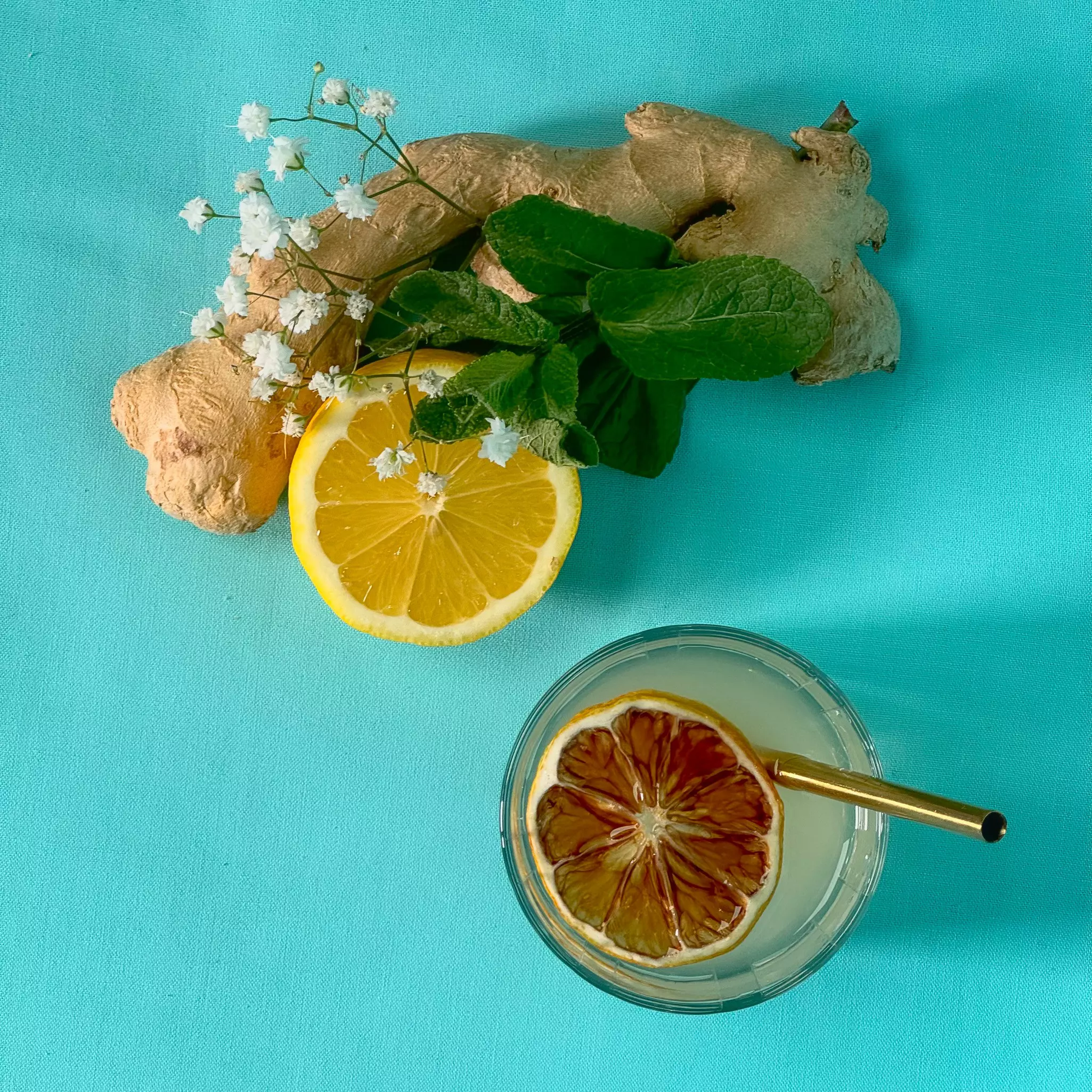 A lemon, ginger and mint on a turquoise tablecloth.