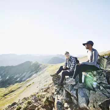 Smiling couple hanging out on rocks during early morning hike in mountains