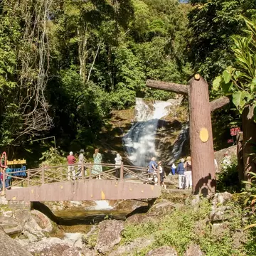 Lata Iskandar waterfall tumbling over rock through rainforest, with a wooden footbridge and visitors in Perak, Malaysia