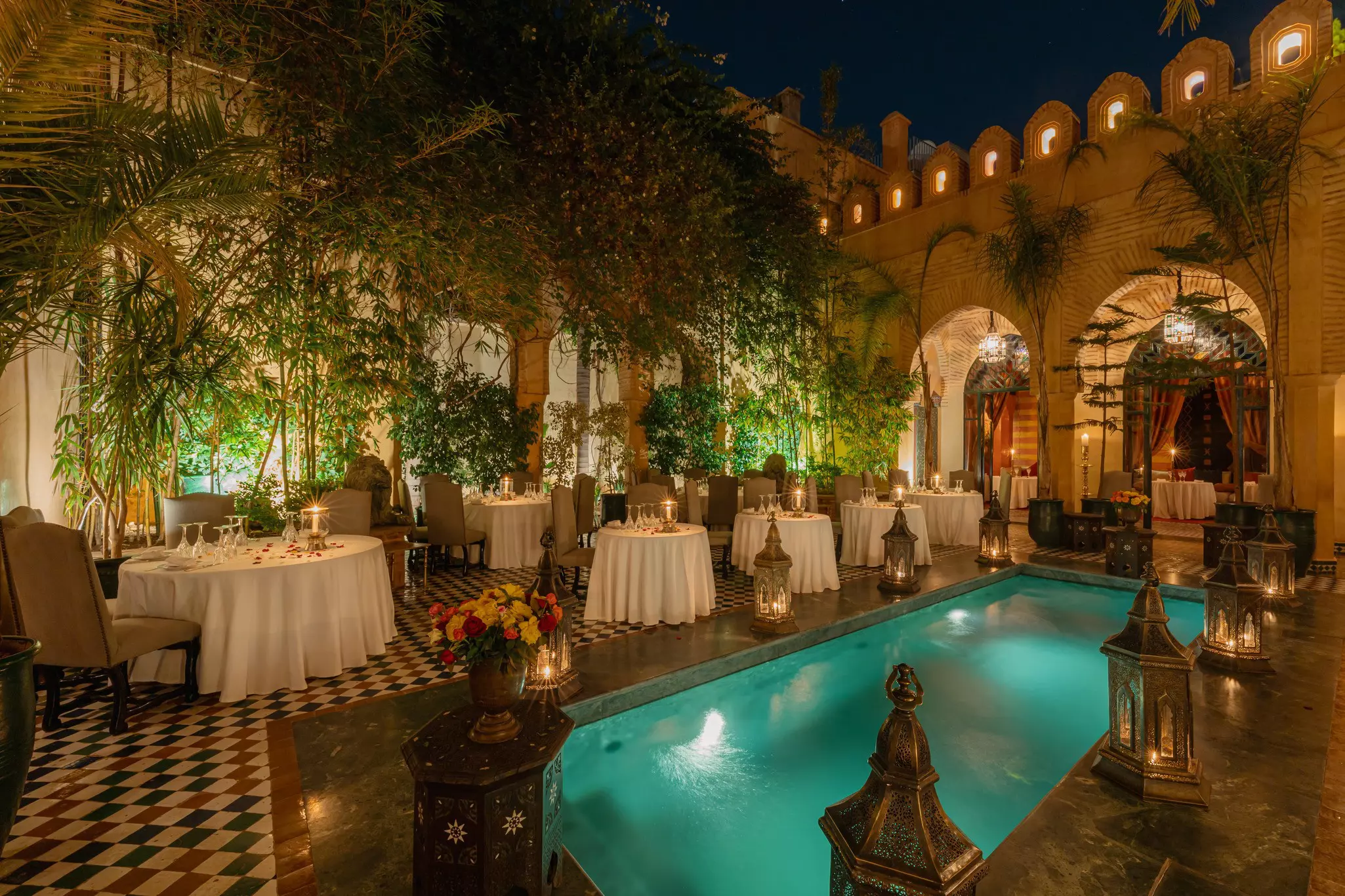 Tables and chairs in a courtyard with a small pool glowing in the candlelight.