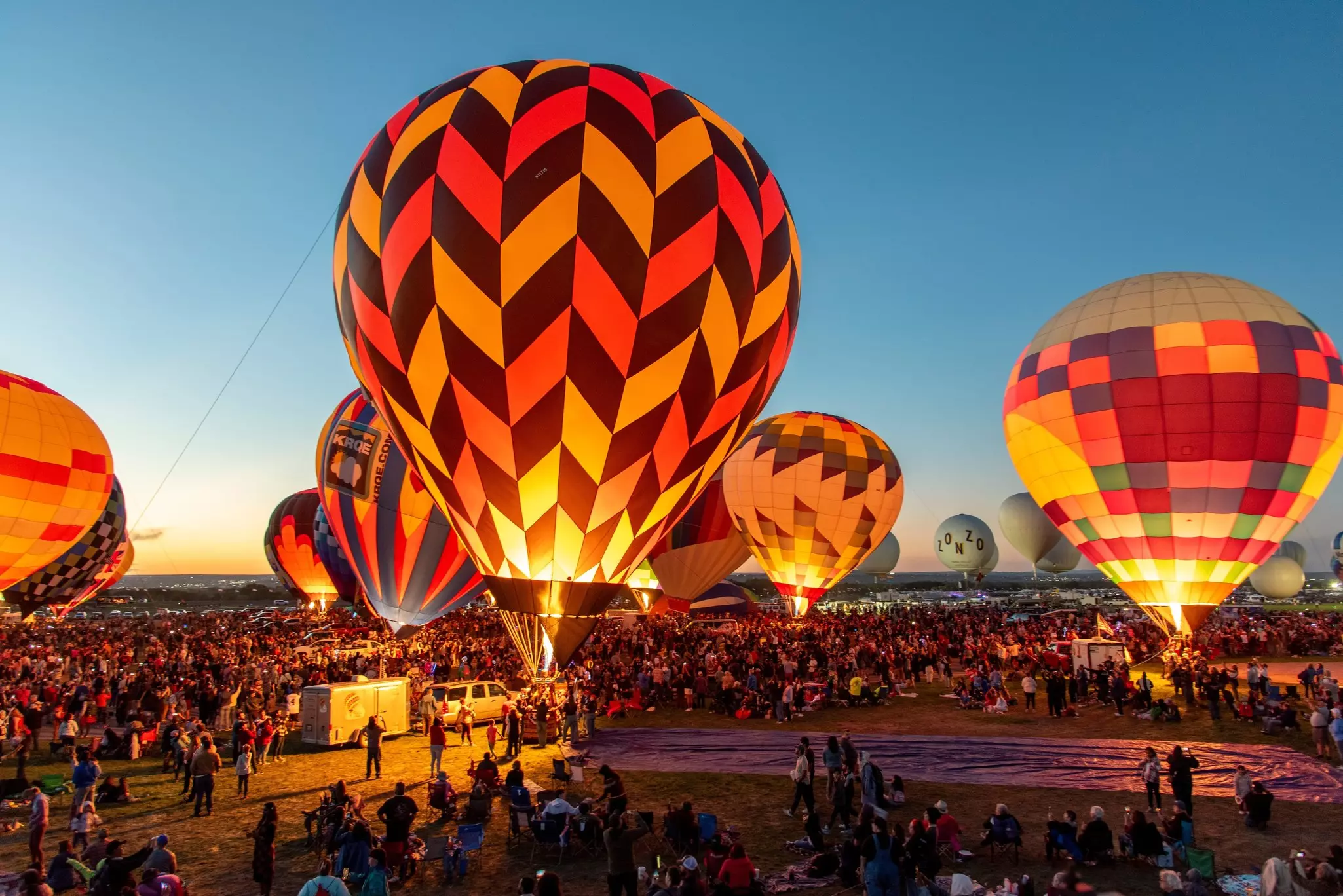 Large hot air balloons being lit up surrounded by a crowd.