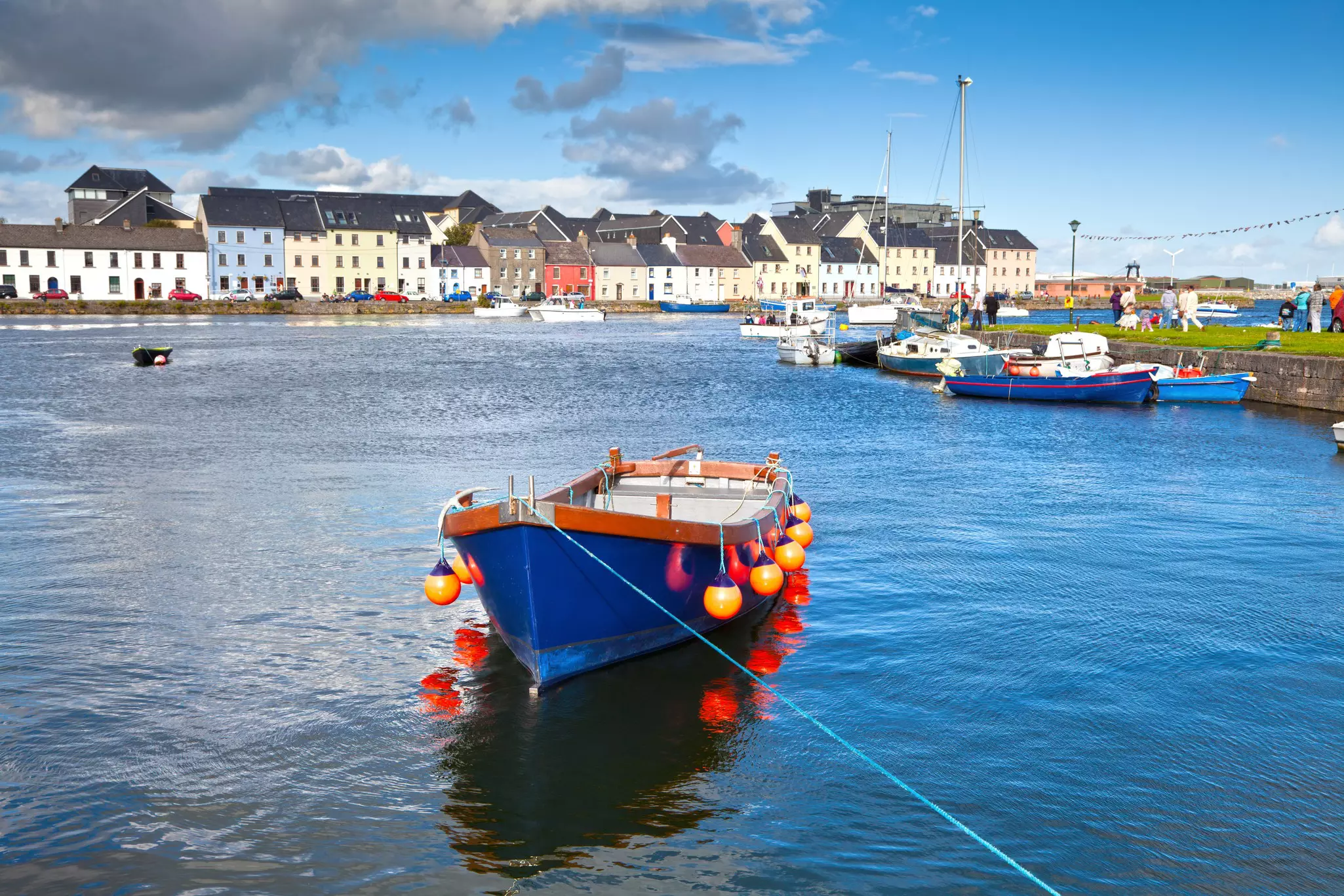A blue boat in Galway Bay in front of the pastel buildings of the old town.