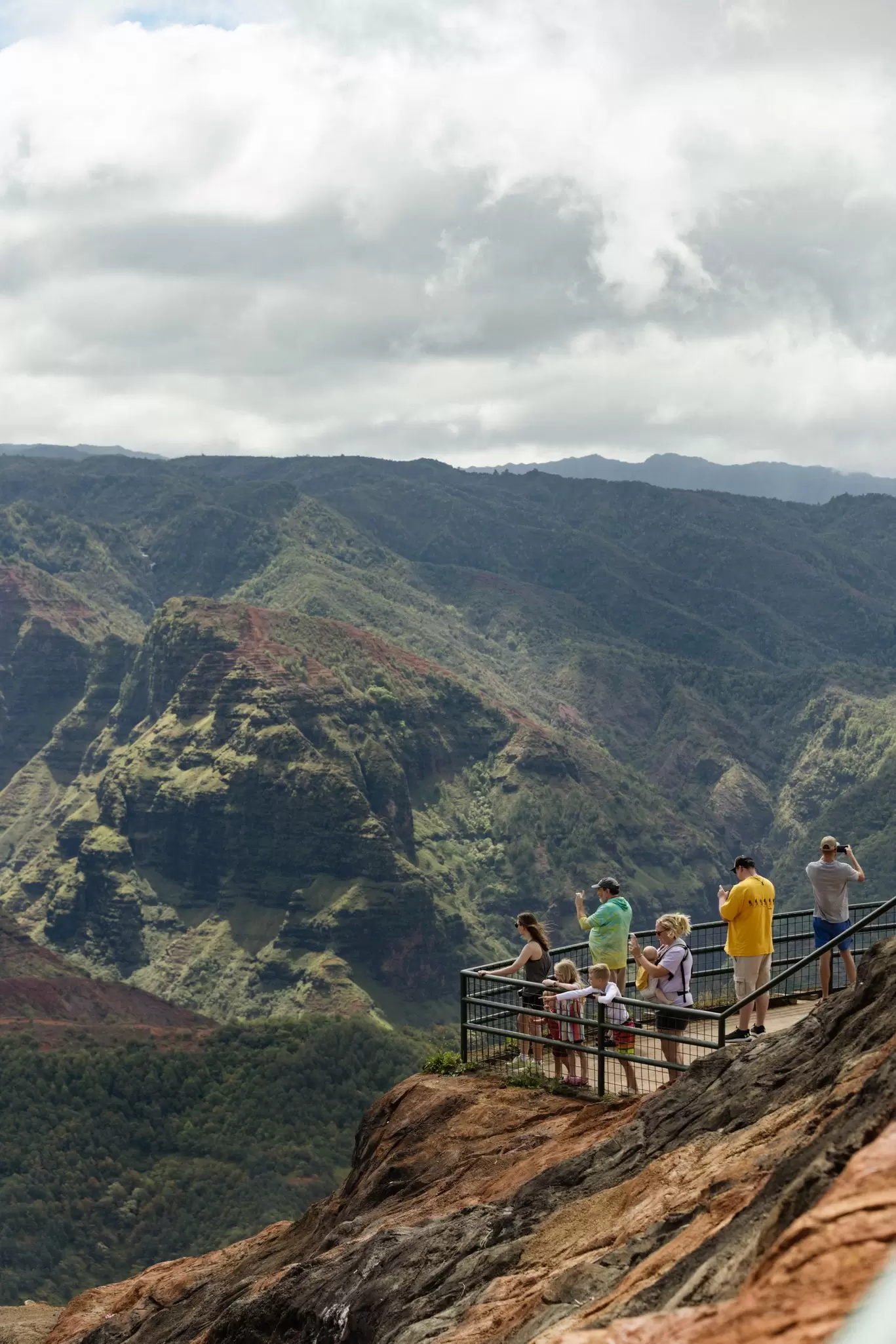People look and take pictures of a large green canyon in Hawaiʻi.