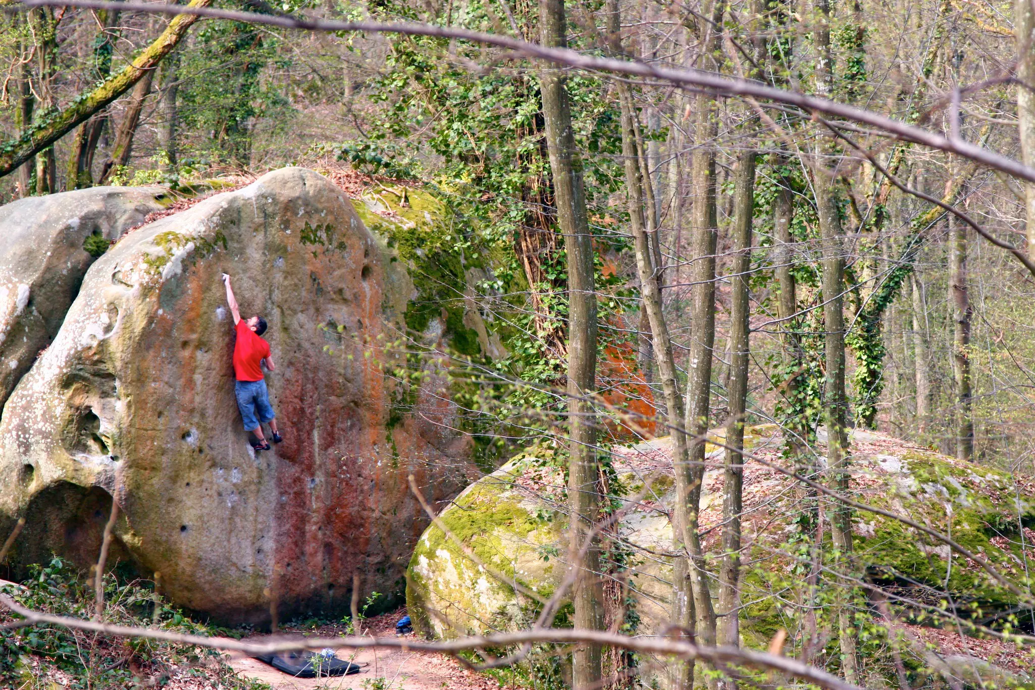 A rock climber reaches high on a large boulder