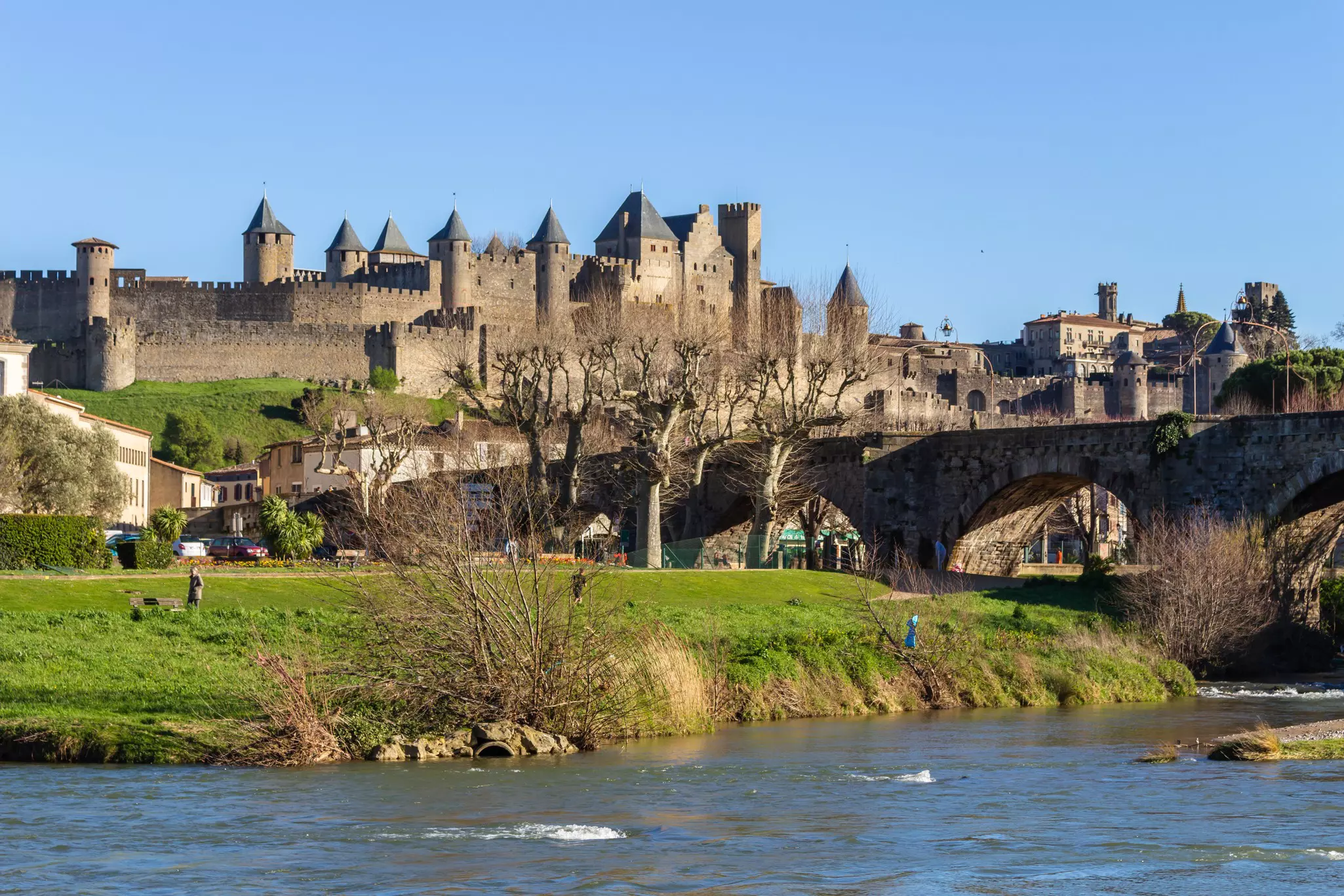 A stone bridge crosses a river leading to a vast fortified castle.
