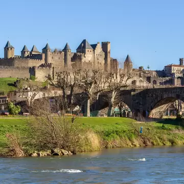 A stone bridge crosses a river leading to a vast fortified castle.