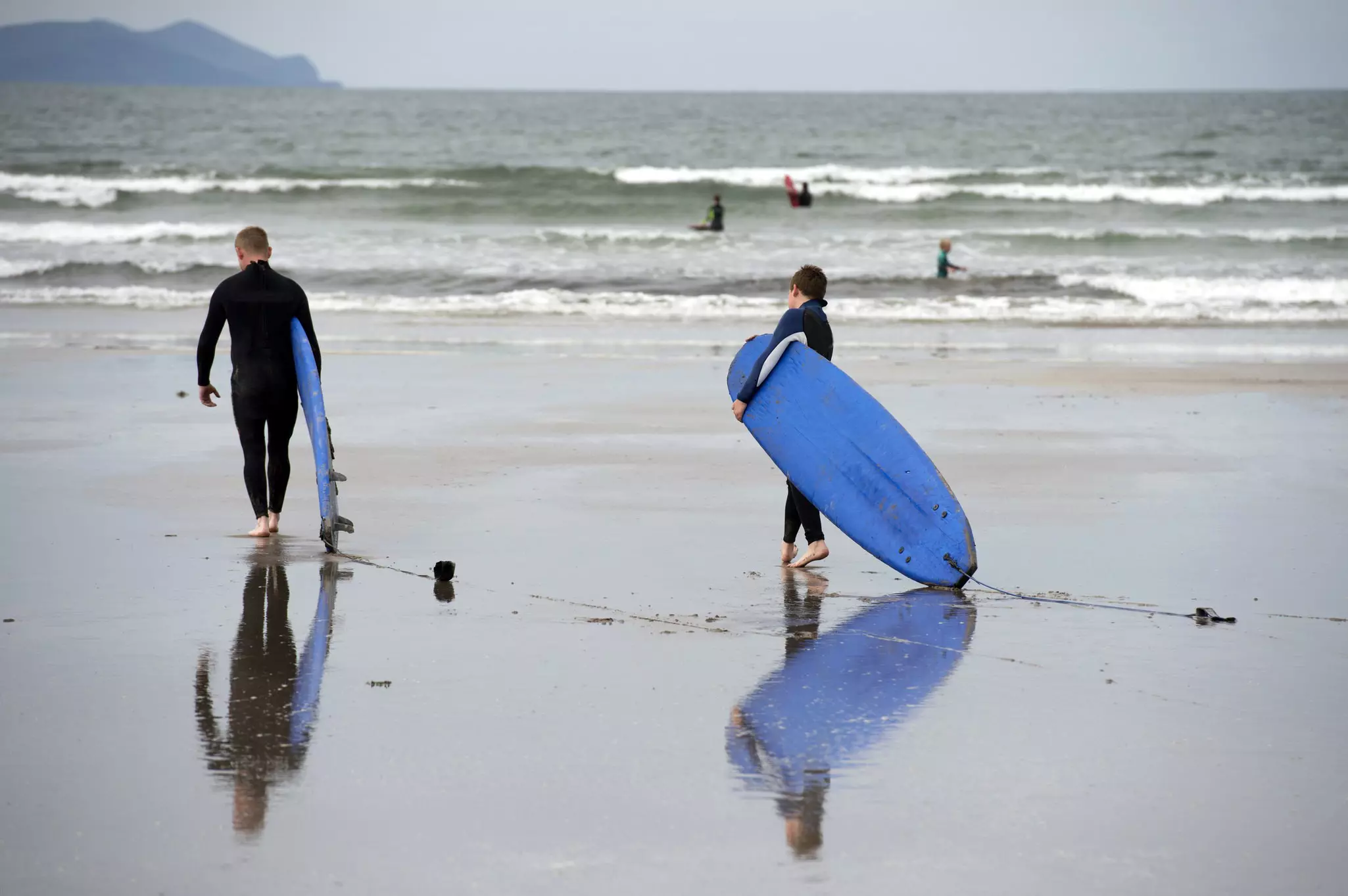 Two surfers with surfboards on the sand at Inch Beach on the Dingle Peninsula in Ireland.