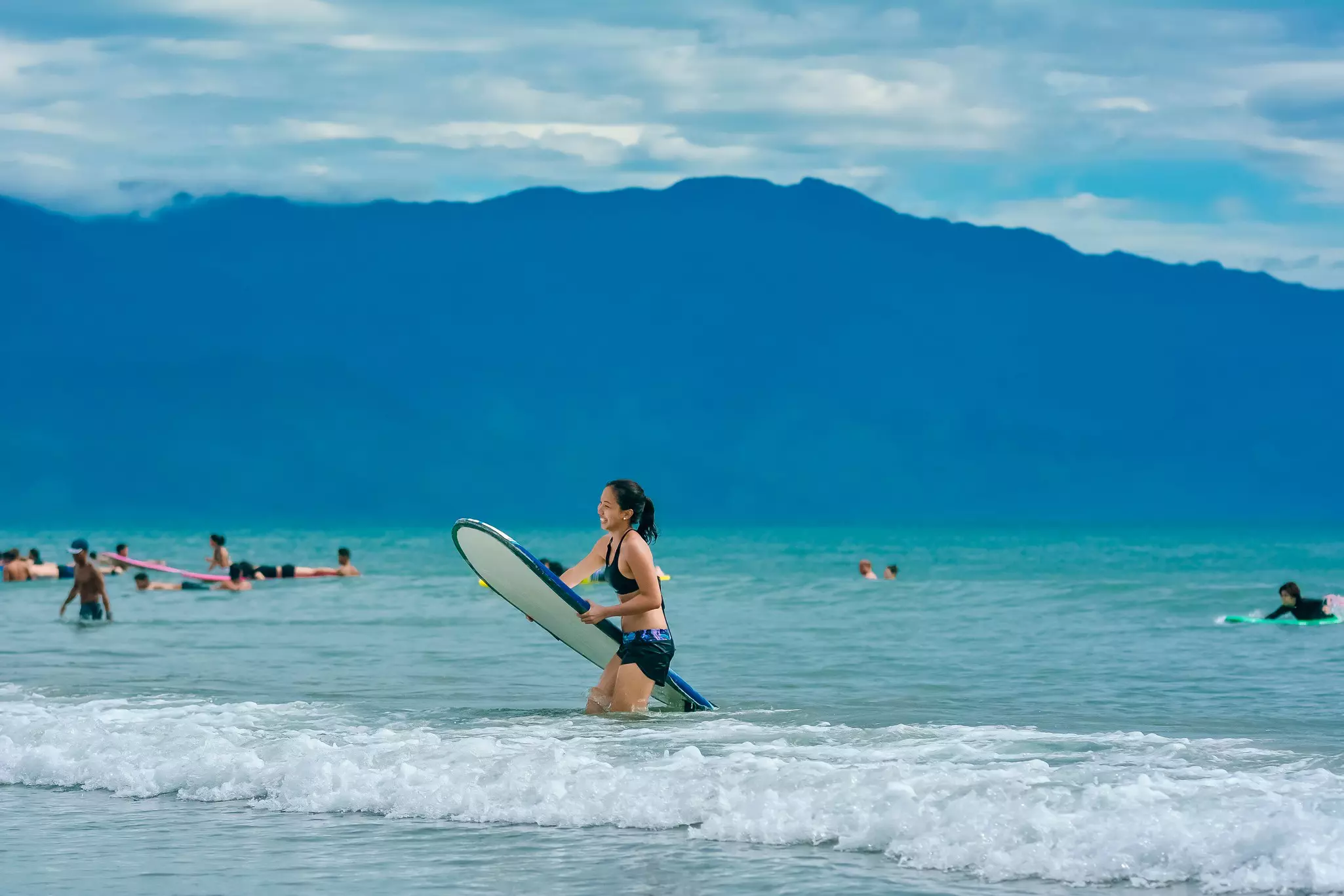 A woman smiles as she heads out of the sea carrying her surfboard.
