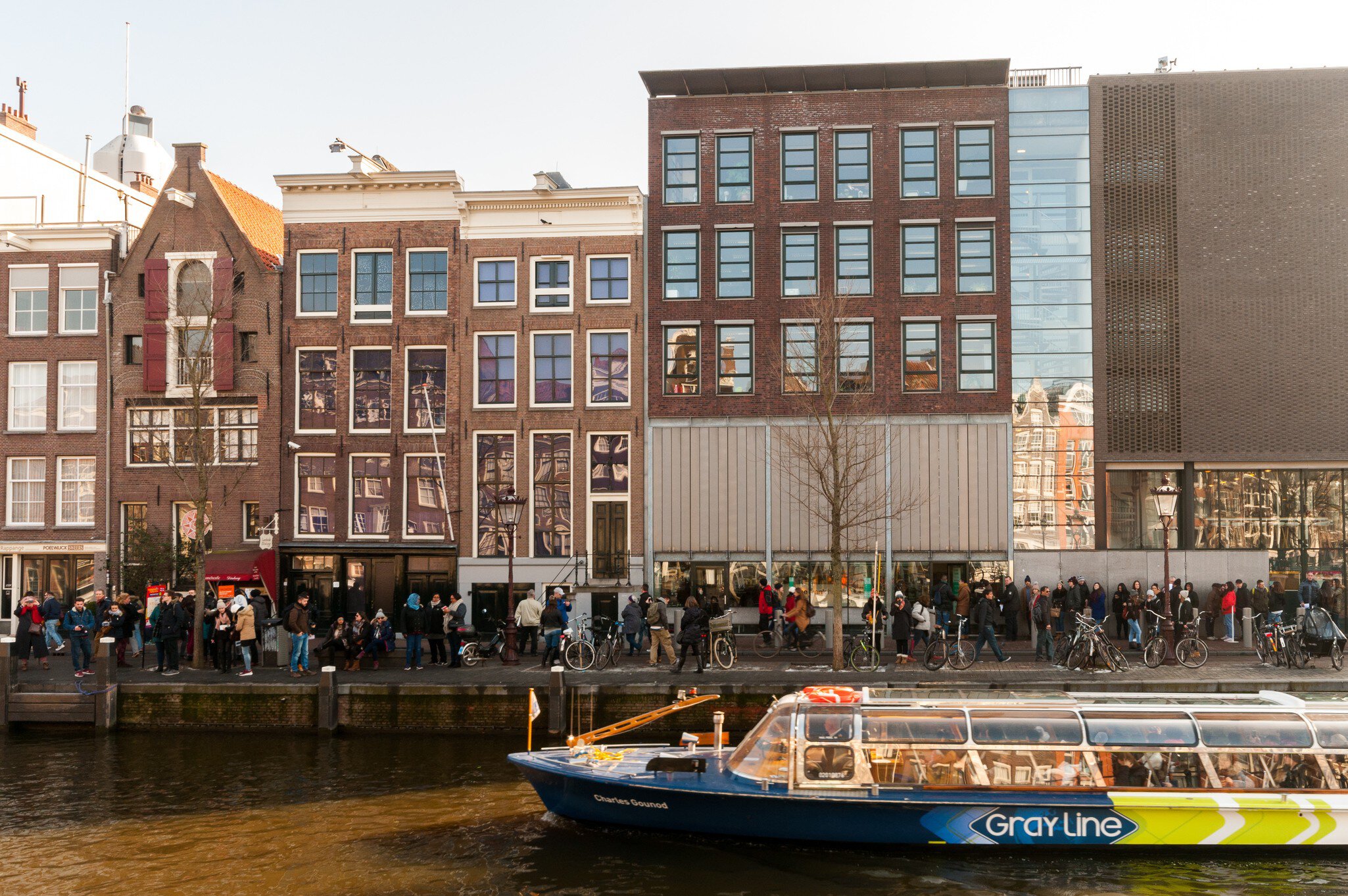 February 13, 2018: Queue of people waiting to enter the Anne Frank museum house, with a passing tour boat on the canal.