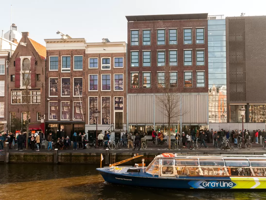 February 13, 2018: Queue of people waiting to enter the Anne Frank museum house, with a passing tour boat on the canal.