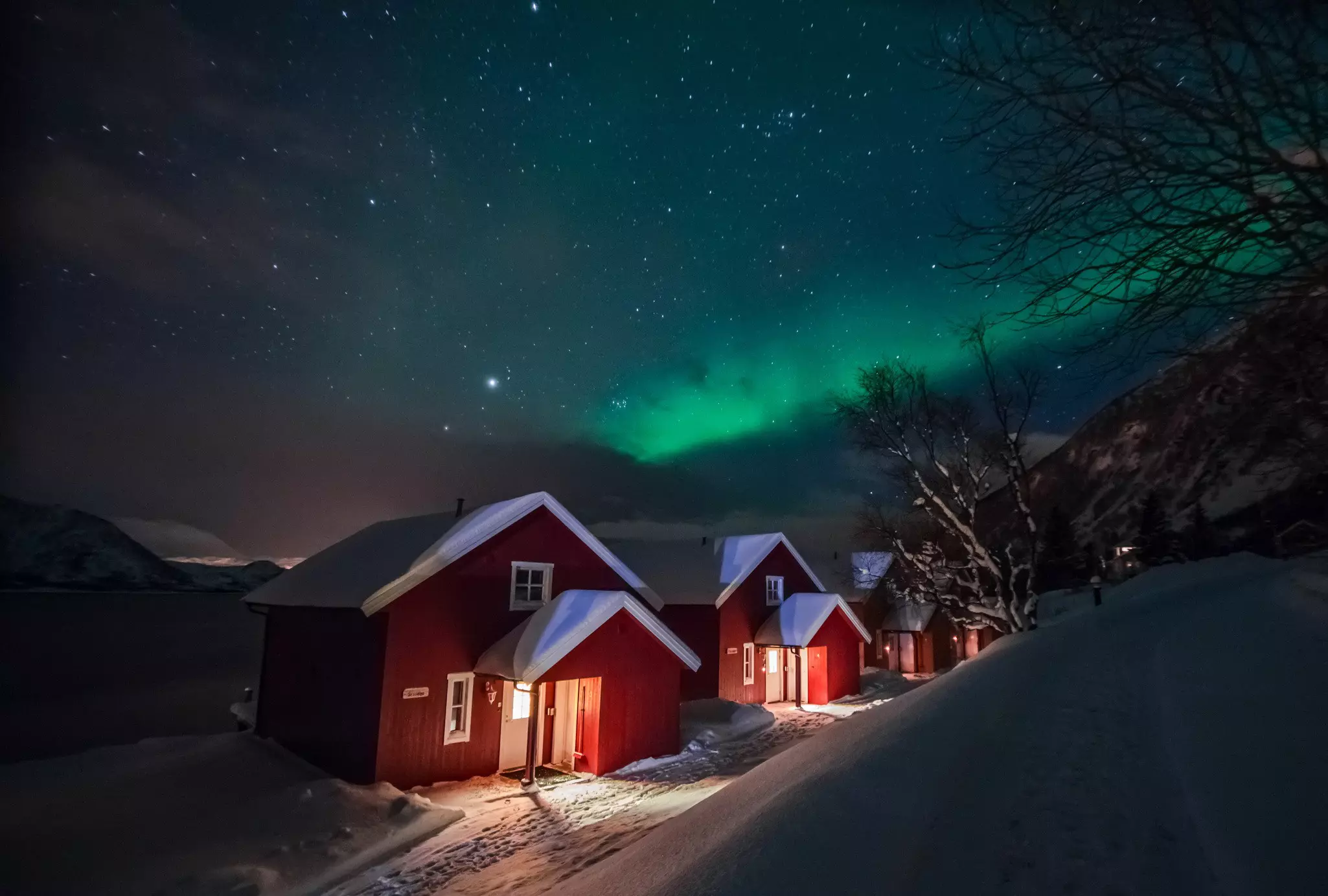 Northern lights (Aurora Borealis) over the red snowed-in cottages in a Lapland village.