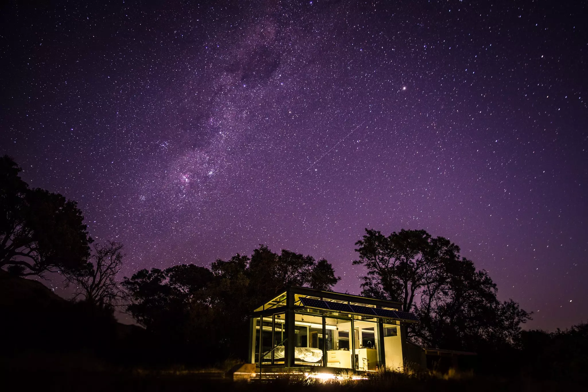 A glass cabin under a night sky full of stars.