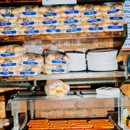 hot dogs on a roller grill with three shelves of plastic-wrapped hot dog buns