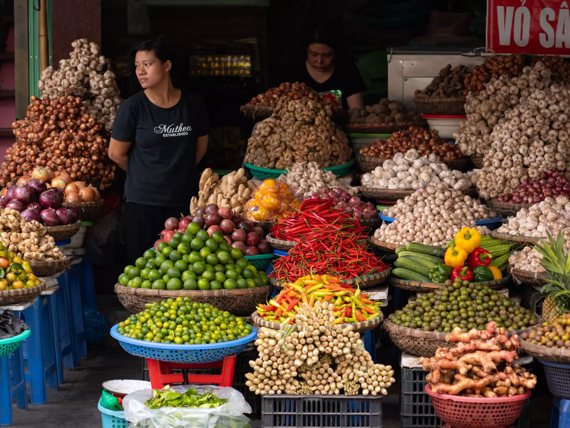 Two people standing by a display of produce and spices in baskets 